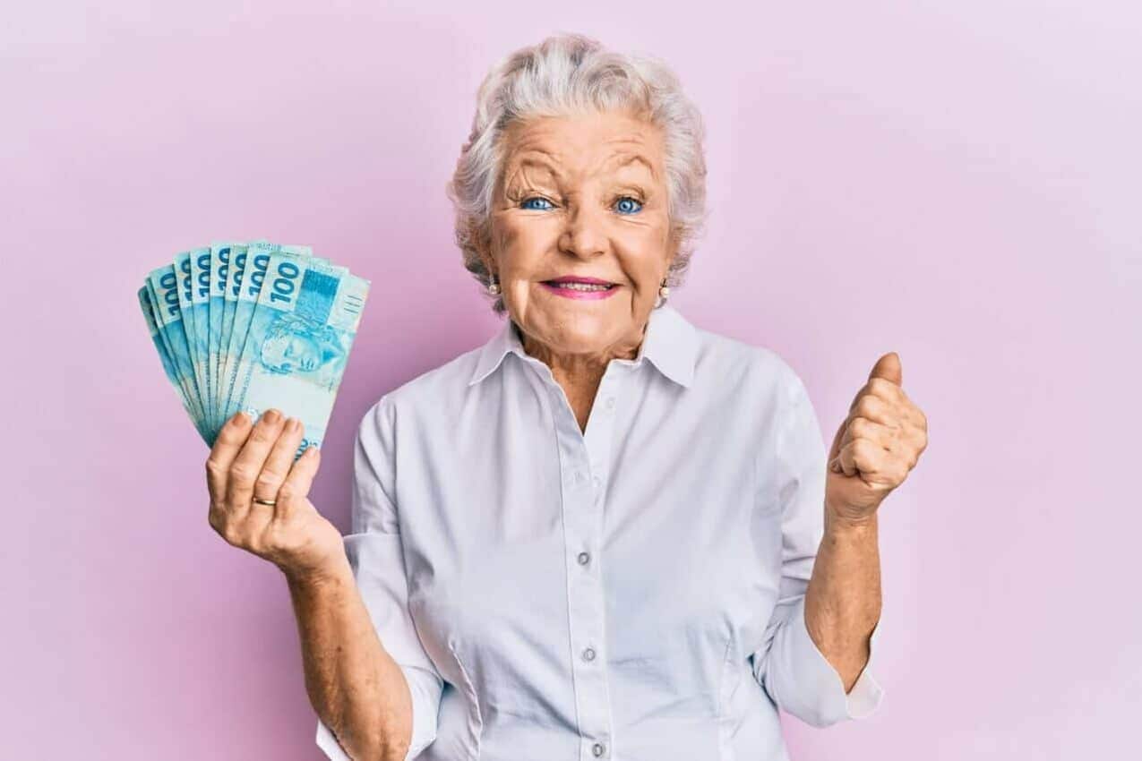 Idosa aposentada com notas de 100 reais na mão enquanto sorri