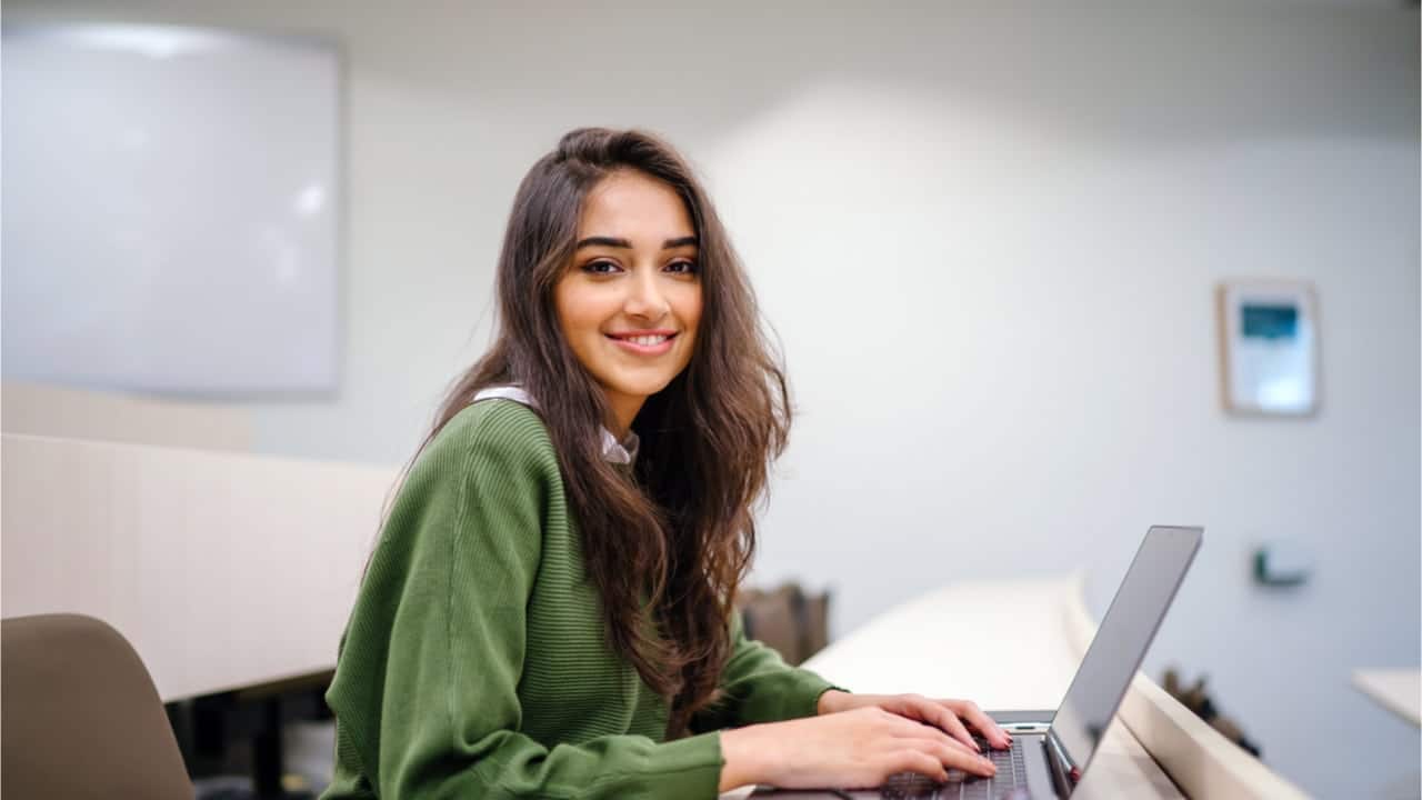 Jovem sorrindo e mexendo no computador em escritório