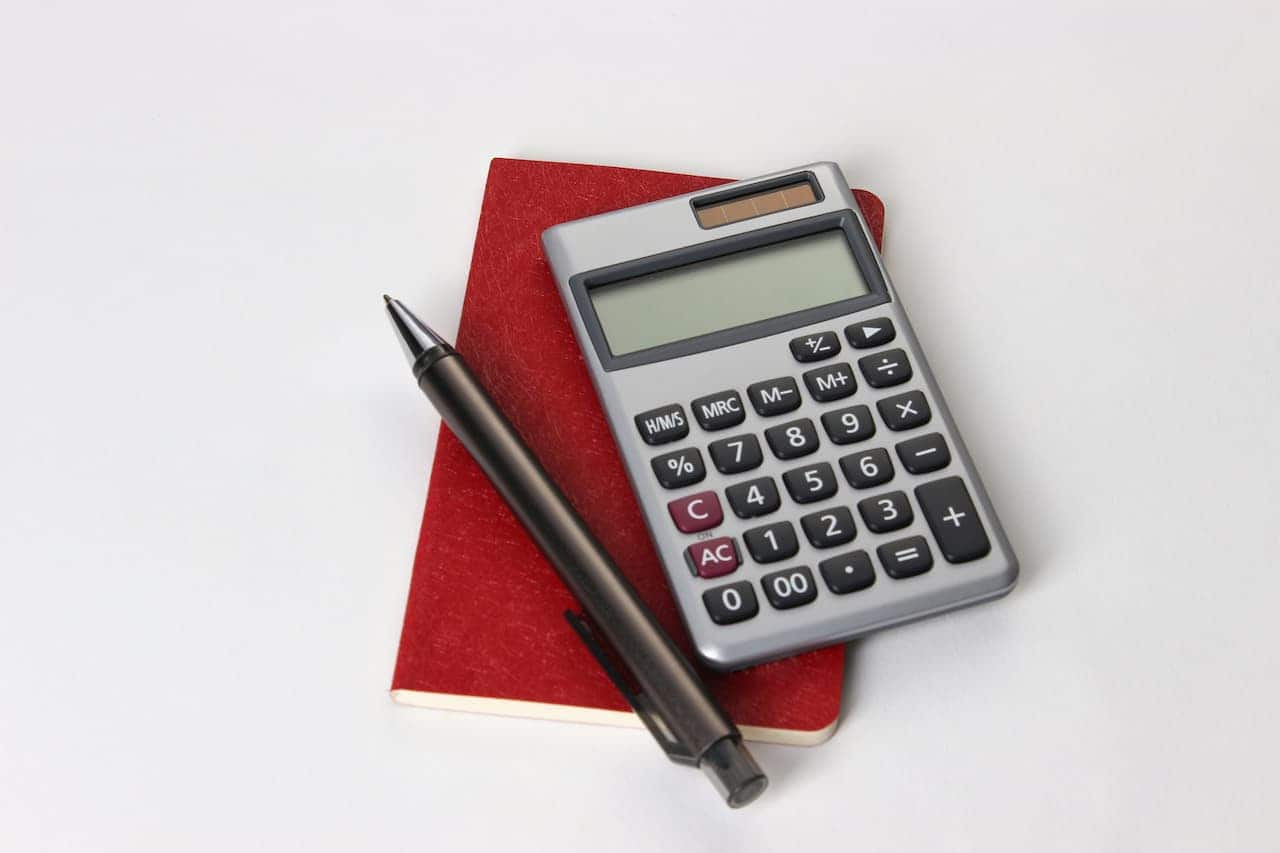 Imagem de uma calculadora e uma caneta em cima de um caderno em um fundo branco
