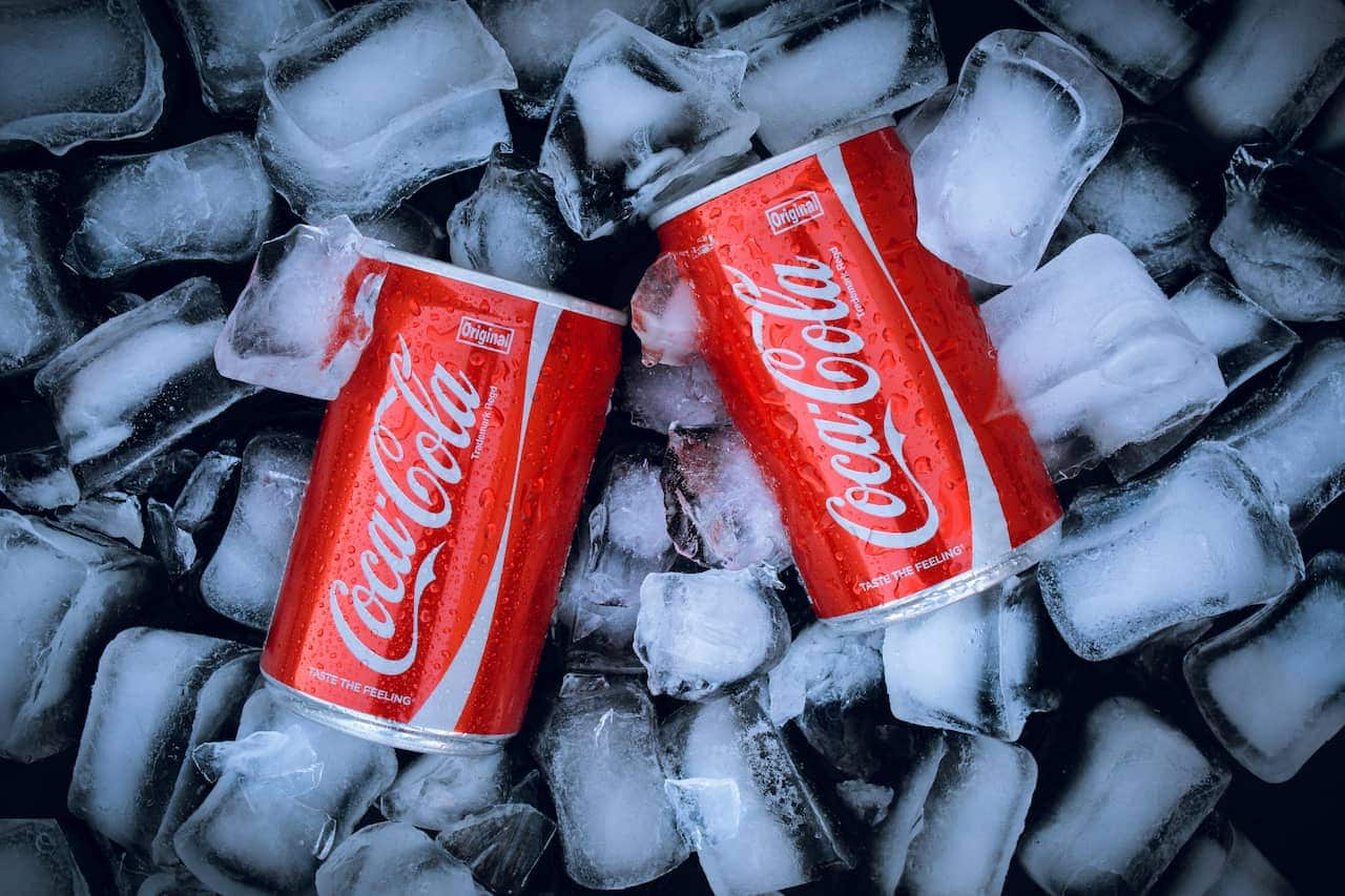 Imagem de duas latas de coca-cola em cima de várias pedras de gelo