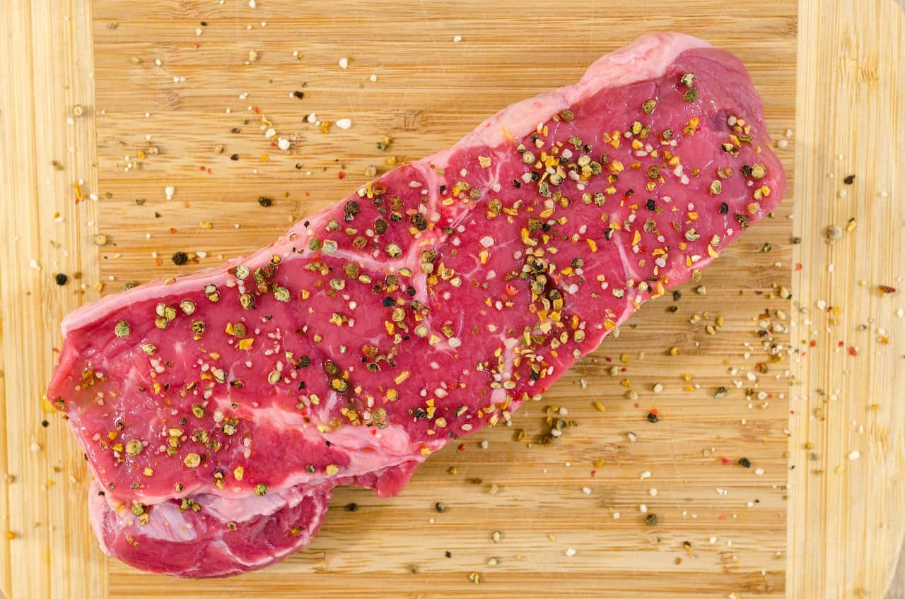 Imagem de uma carne crua tempeada em cima de uma tábua