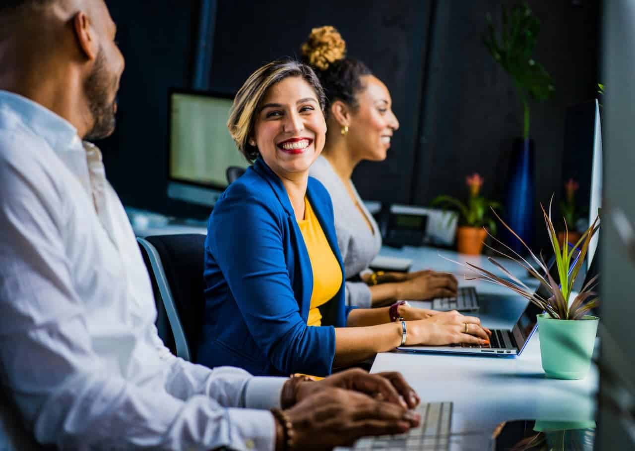 Imagem de três pessoas sorrindo, cada um em frente a um notebook