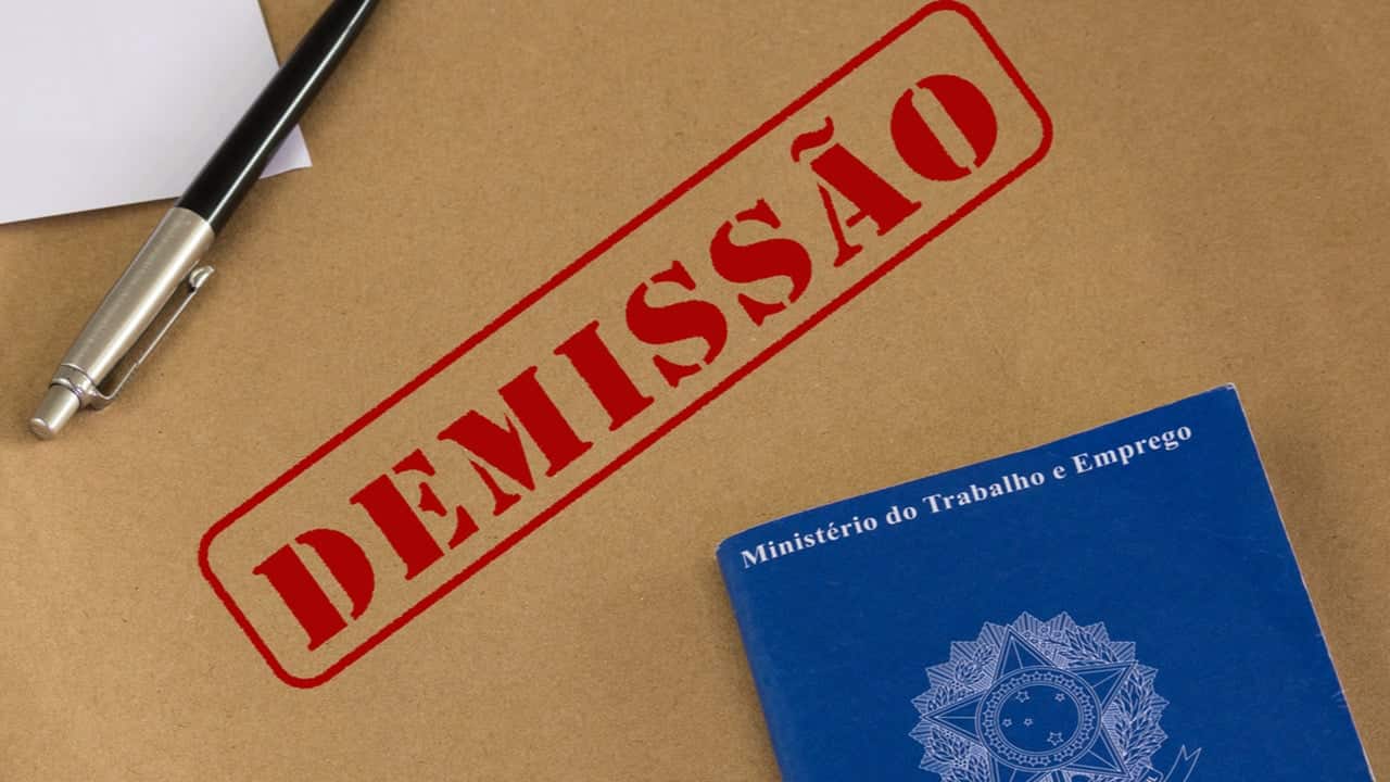 Superfície carimbada com a palavra demissão. Ao lado, uma caneta e uma Carteira de Trabalho.