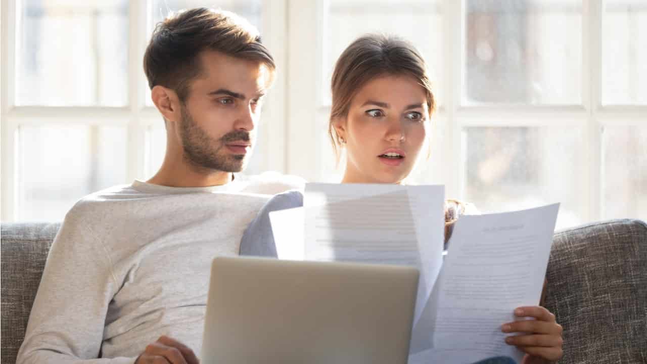 Casal com contas na mão de frente a um computador analisando a melhor maneira de pagar as contas