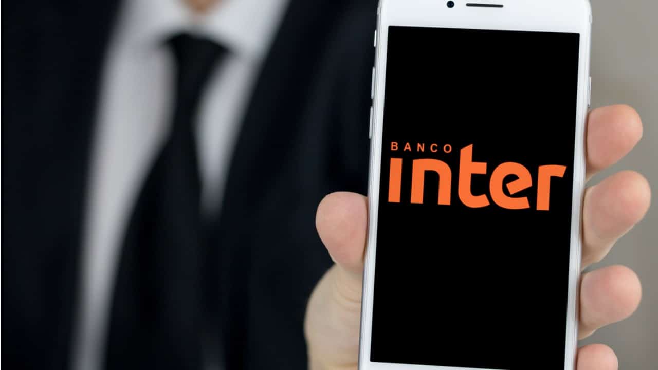 homem de terno e gravata segurando um celular que mostra a tela inicial do aplicativo do banco Inter