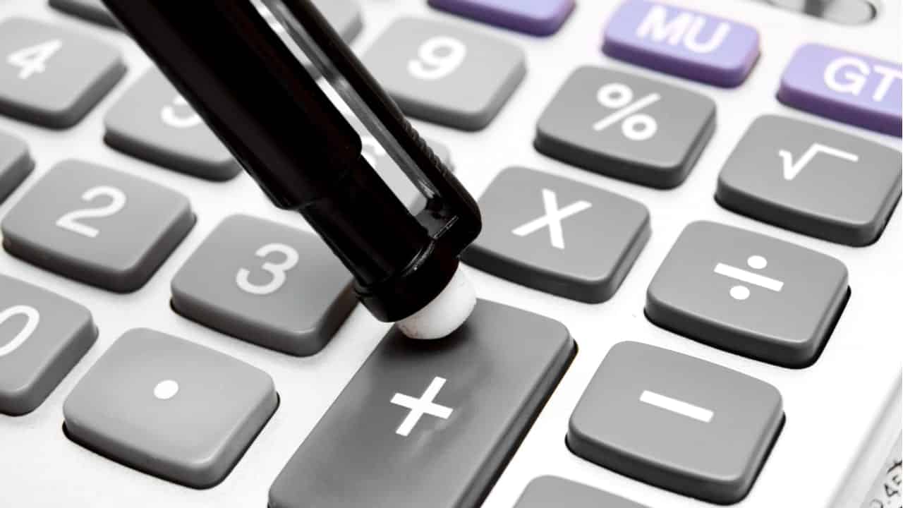Ponta de caneta apertando sinal de "+" da calculadora com vistas à gestão financeira