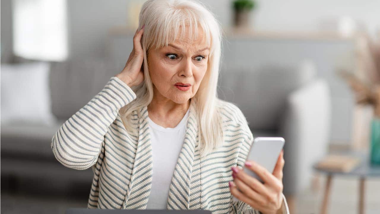 Imagem de senhora de meia idade olhando para seu celular com semblante de susto