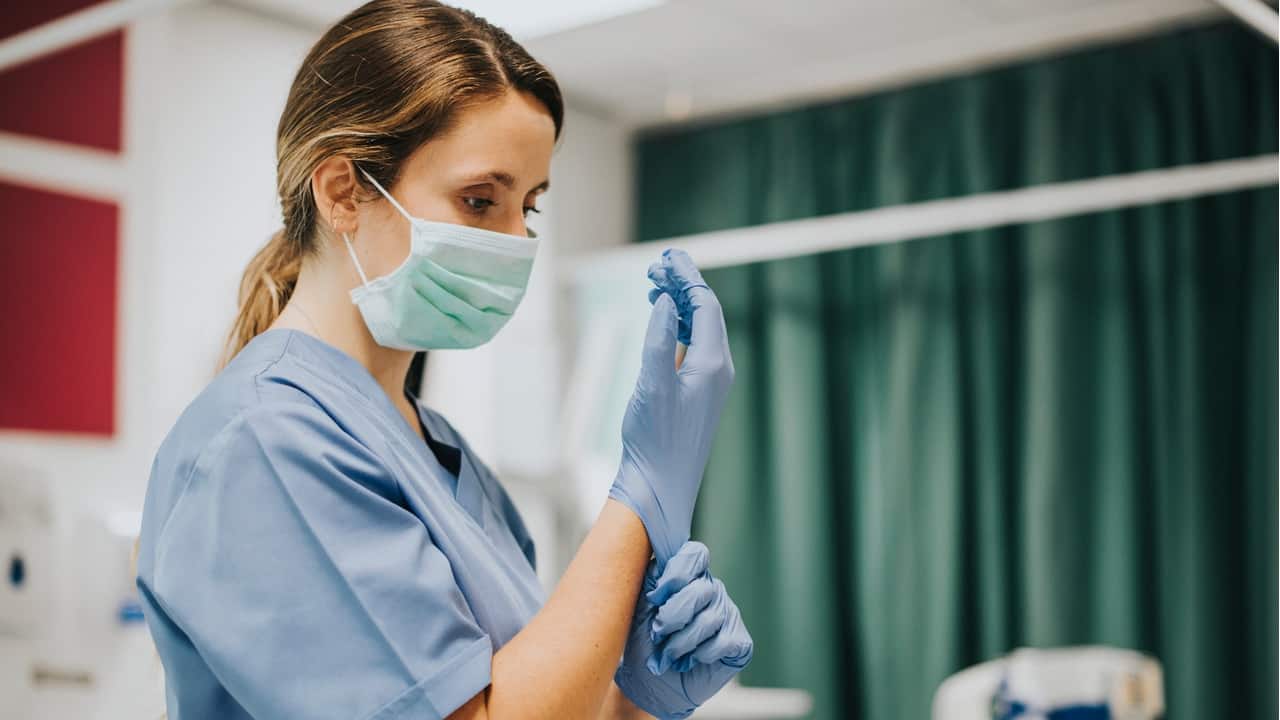 Profissional da saúde colocando luvas cirúrgicas nas mãos.