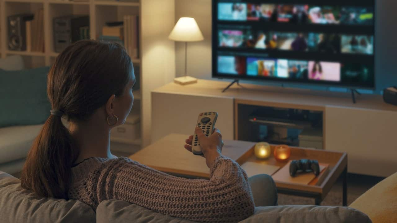 Mulher setnatda no sofá segurando controle de frente para a a tv