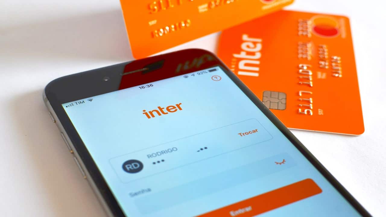Um celular sobre um balcão com o app do Banco Inter aberto e, ao lado, cartões do mesmo banco