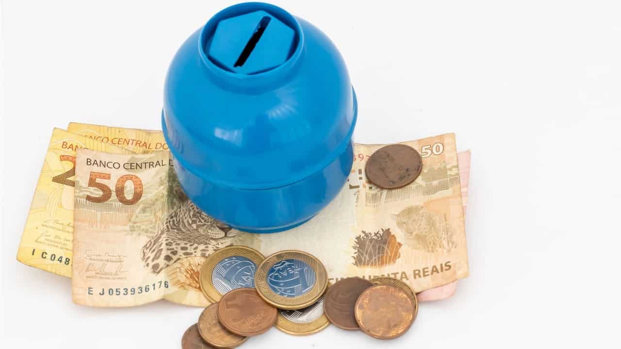 miniatura de botijão de gás em cima de notas de 50 reais e algumas moedas