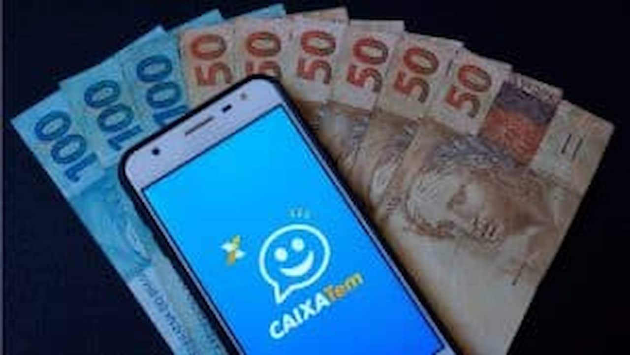 Celular com o aplicativo Caixa Tem na frente de cédulas de real