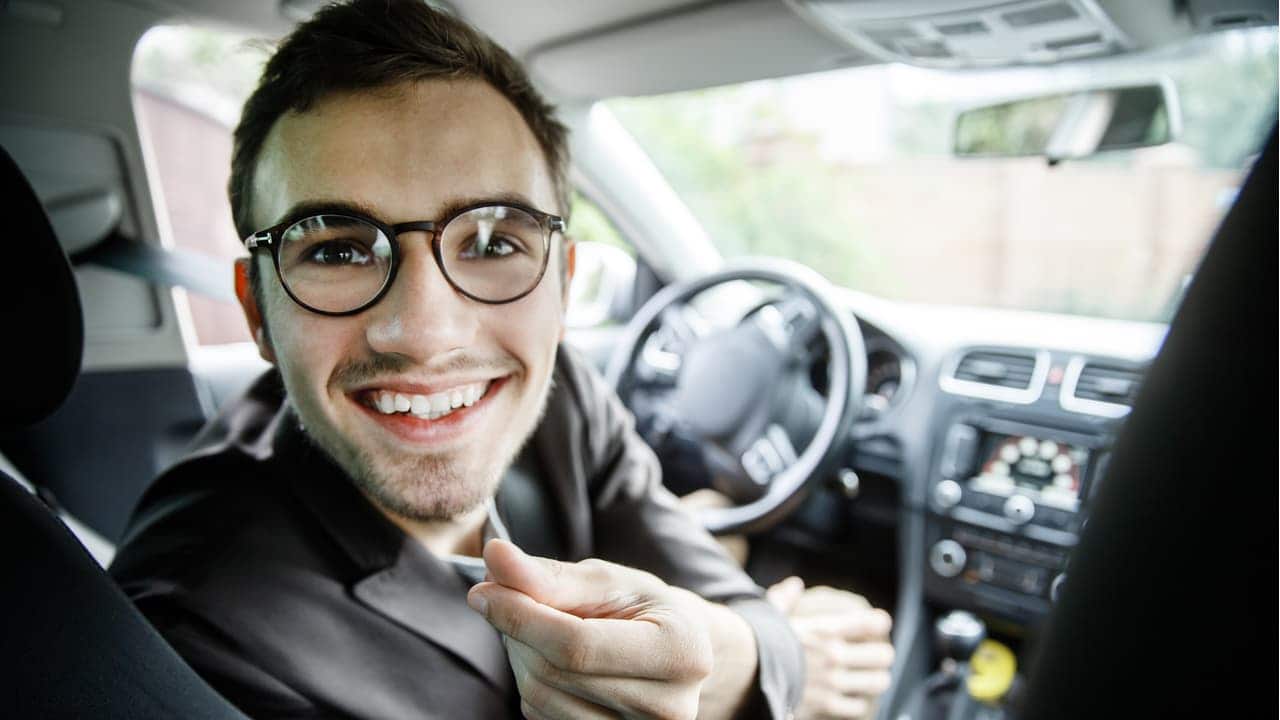 Motorista da Uber dentro de carro fazendo sinal de dinheiro com os dedos