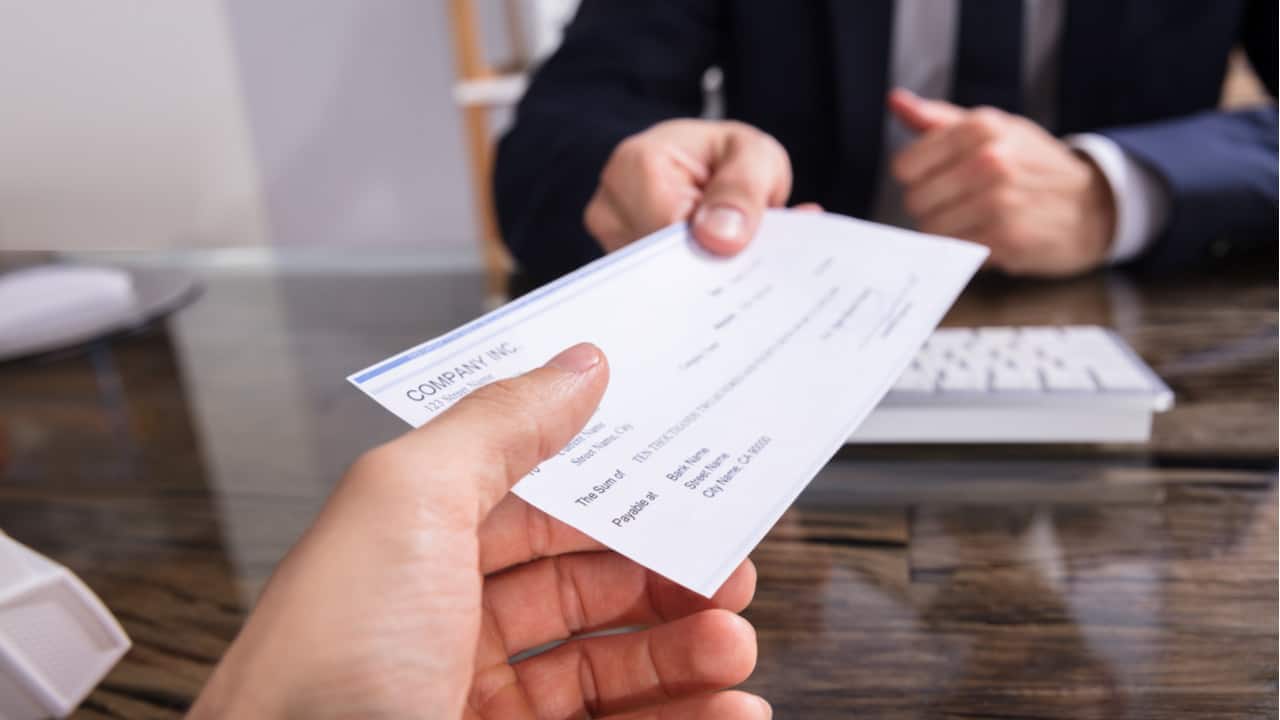 Mão recebendo um cheque de empréstimo ou financiamento das mãos de outra pessoa