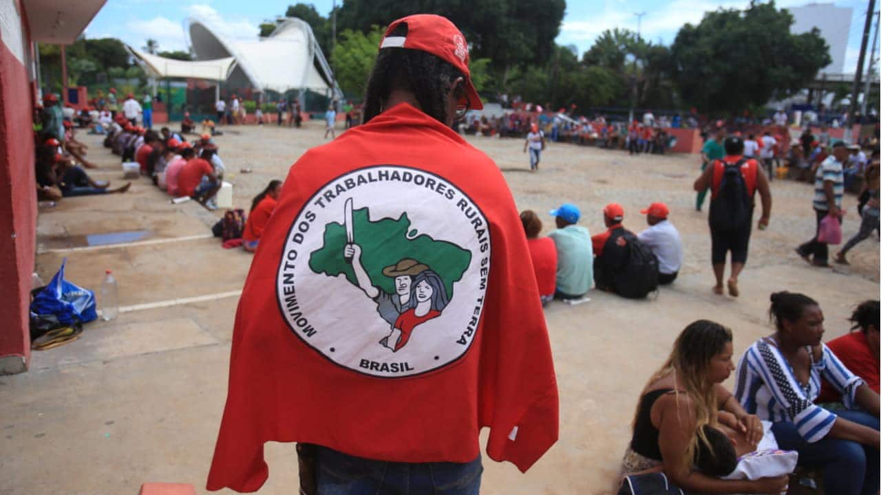 Homem de costas coberto com bandeira do MST (Movimento dos Trabalhadores Rurais Sem Terra)