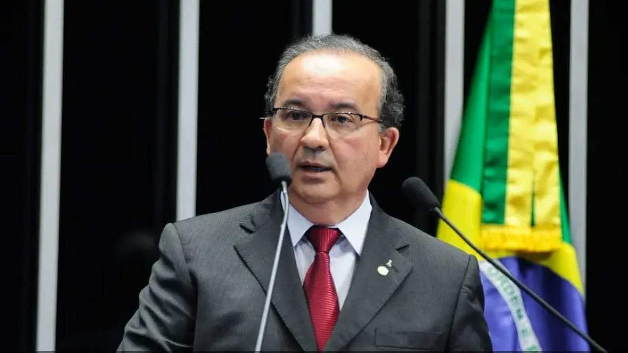 Imagem mostrando governador Jorginho Mello falando em um microfone com a bandeira do Brasil ao lado direito