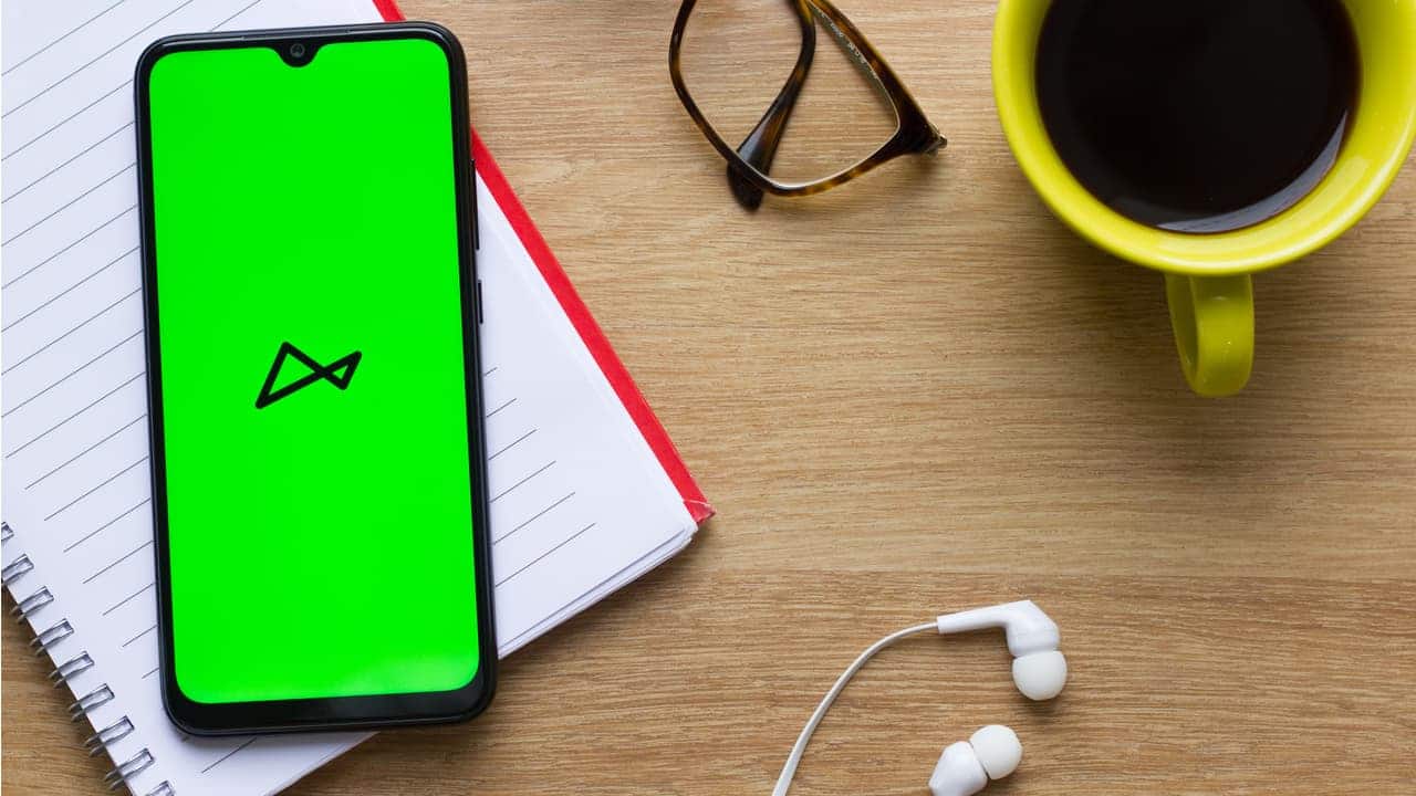 Celular com aplicativo do banco next aberto, ao lado de óculos, fones de ouvido e xícara de café