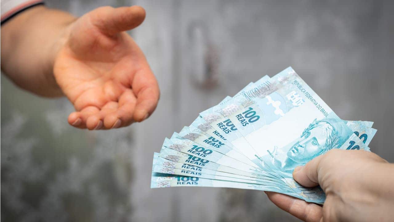 Notas de cem reais sendo oferecidas a uma pessoa