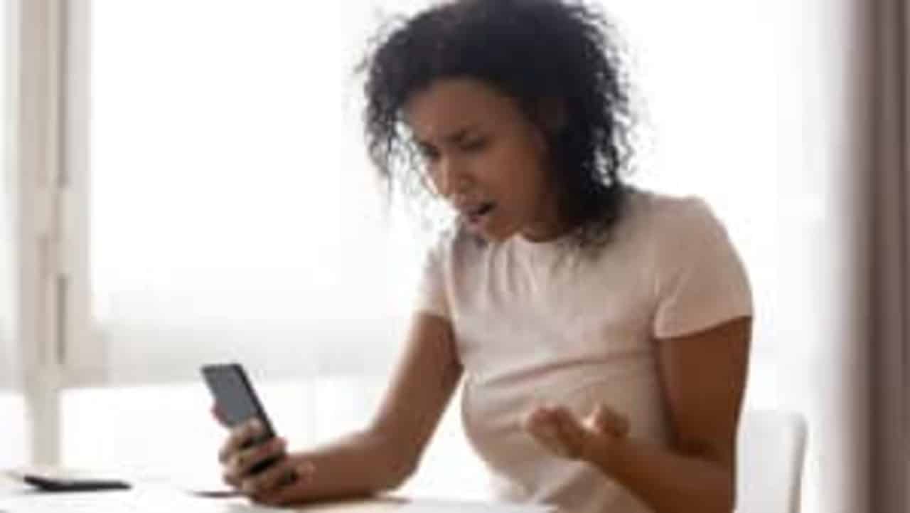 Mulher negra olhando para o celular com expressão de indignação