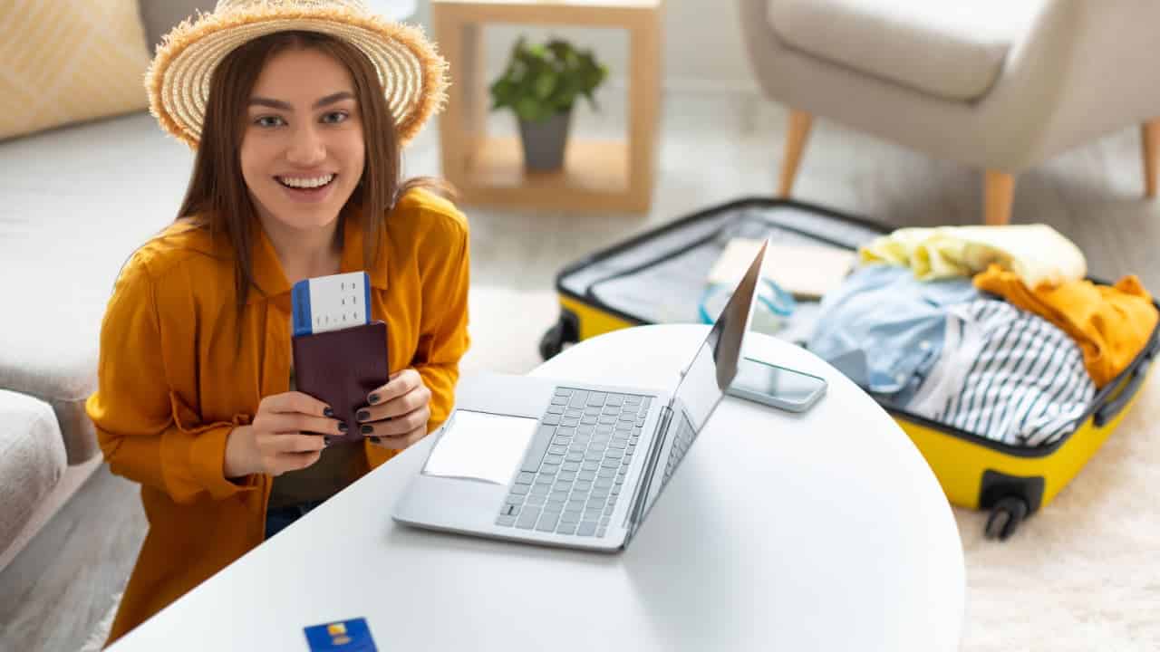 turista solteira sorri comprando passagens de avião em agência de viagens no computador