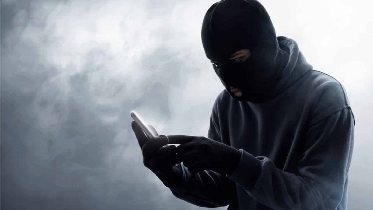 Pessoa encapuzada mexendo em um celular
