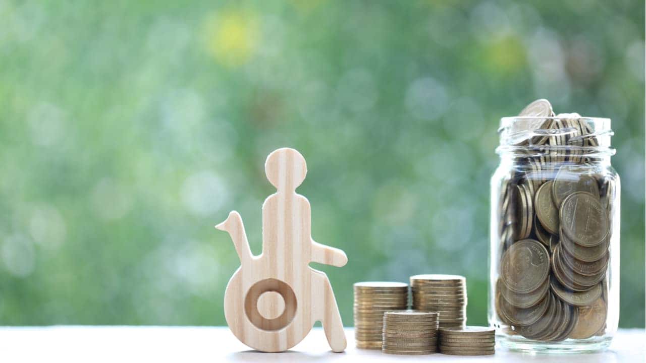 Miniatura com contorno de pessoa com deficiência física em cadeira de rodas. Ao lado, pilhas e um pote de moedas