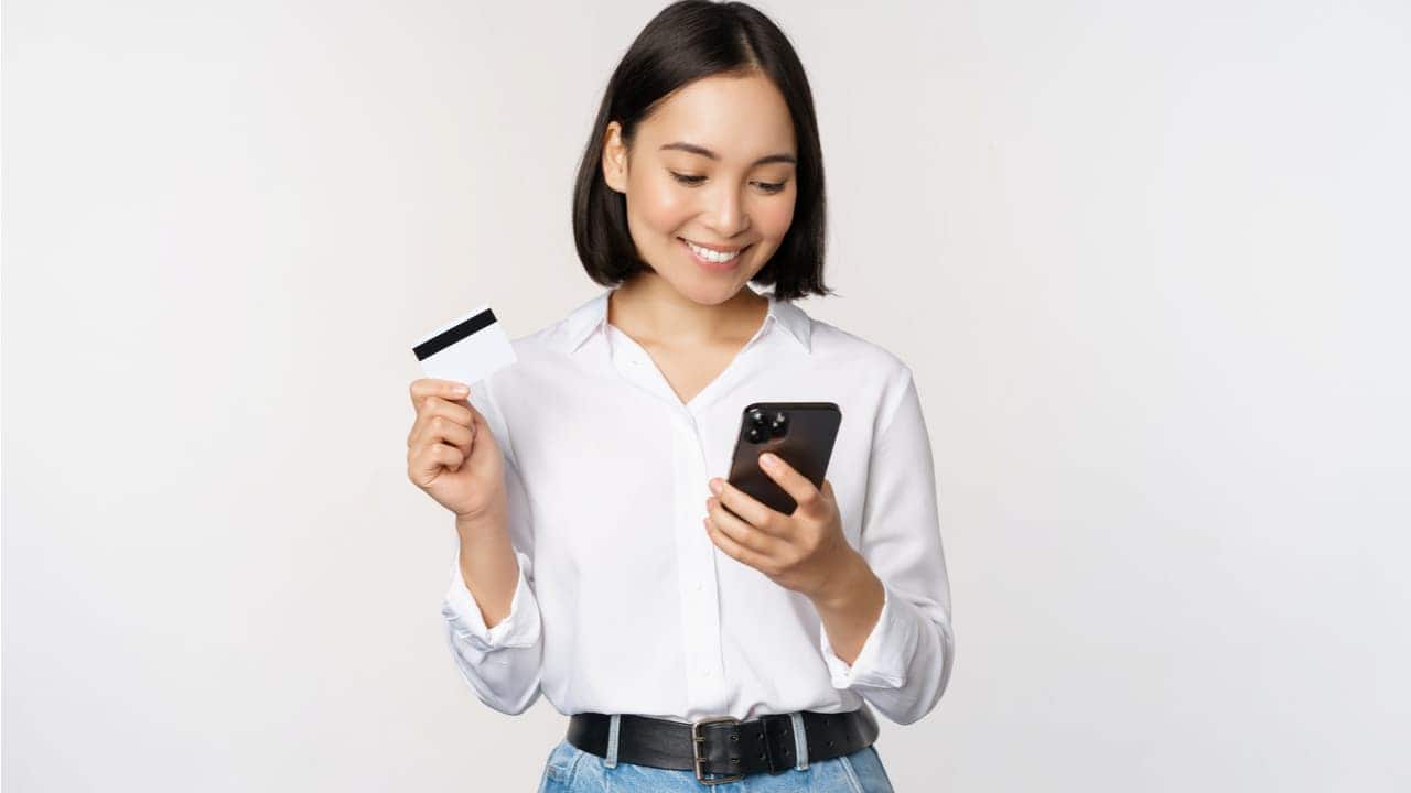 Mulher sorrindo com cartão de crédito e celular em suas mãos