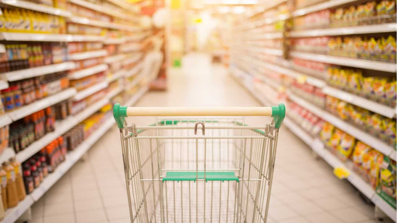 Carrinho de supermercado no centro de um corredor, entre duas fileiras de produtos