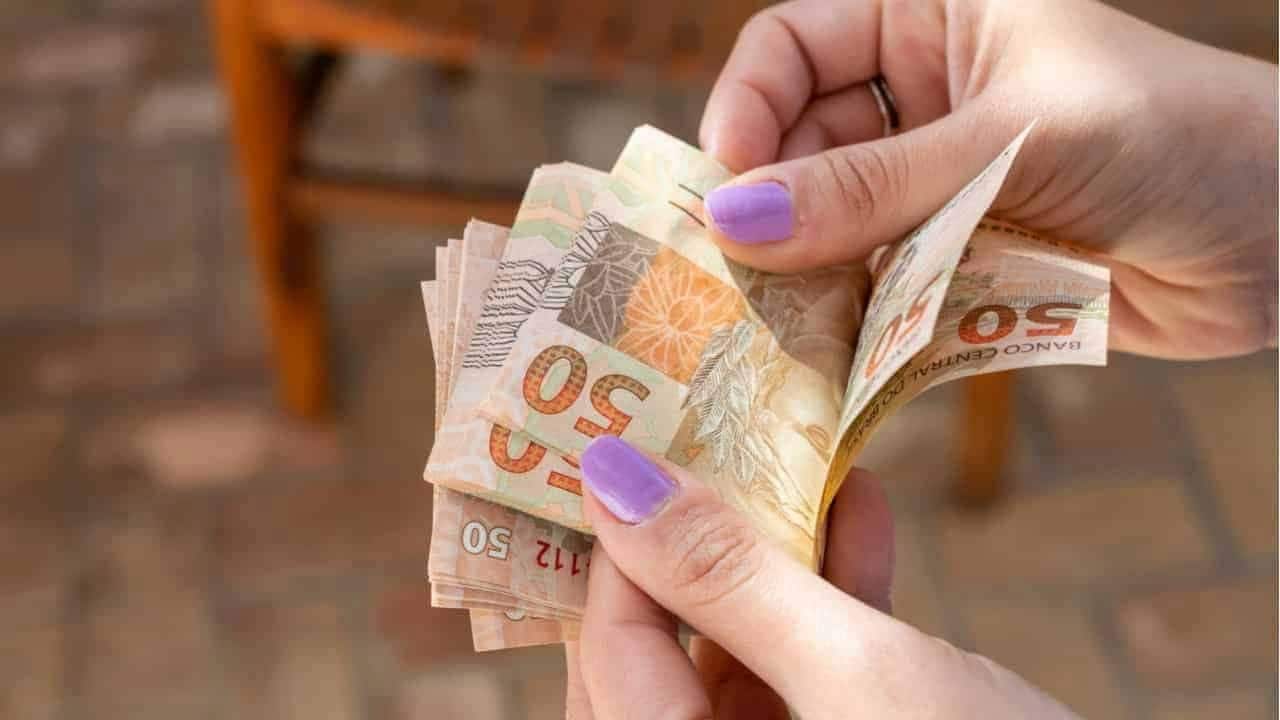 As mãos de uma pessoa com unhas pintadas contando notas de R$ 50