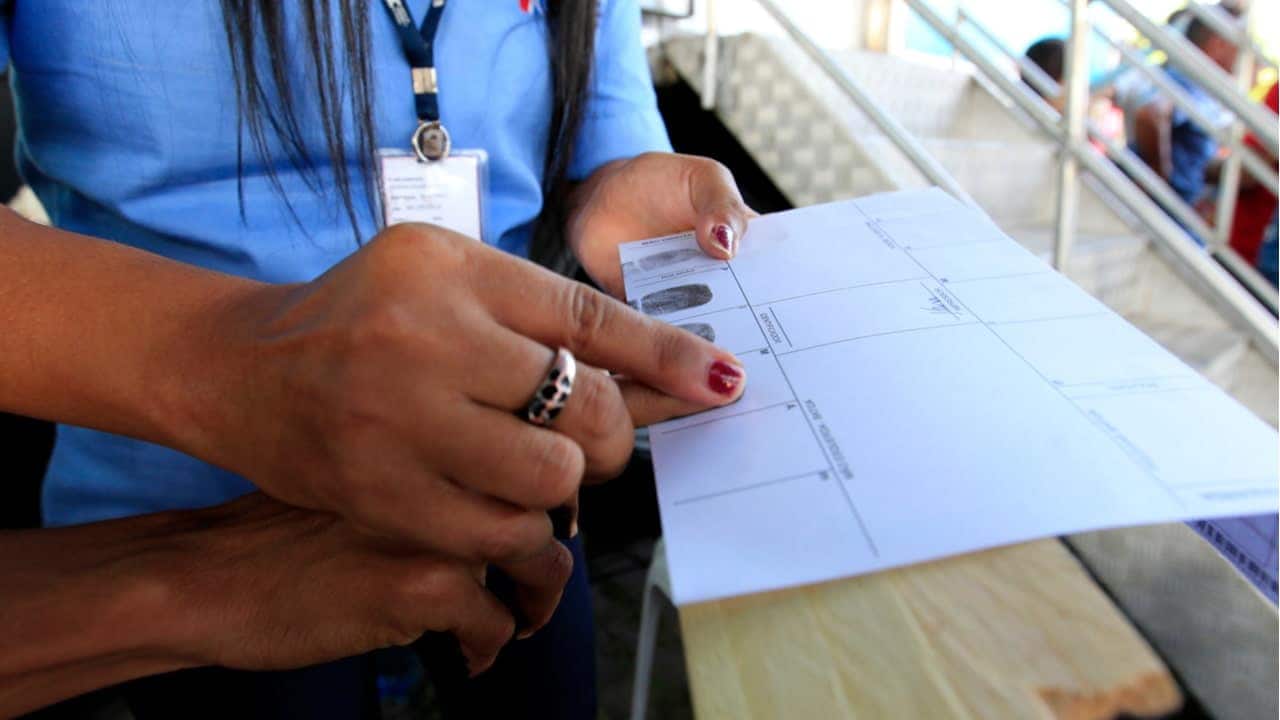 Pessoa tendo impressão digital colhida por outra para emissão de RG