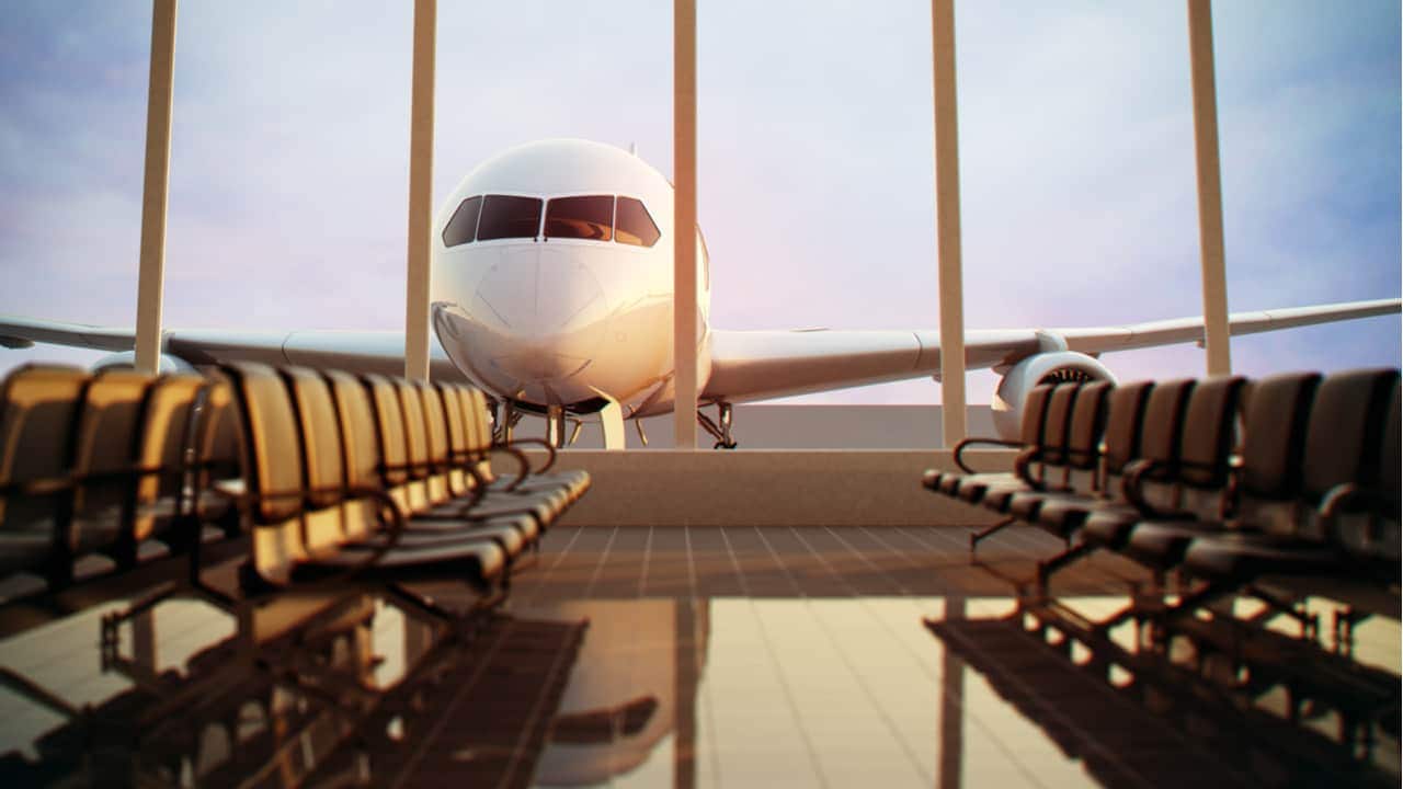 Interior de um aeroporto com cadeiras vazias. Ao fundo, pela janela, um avião parado