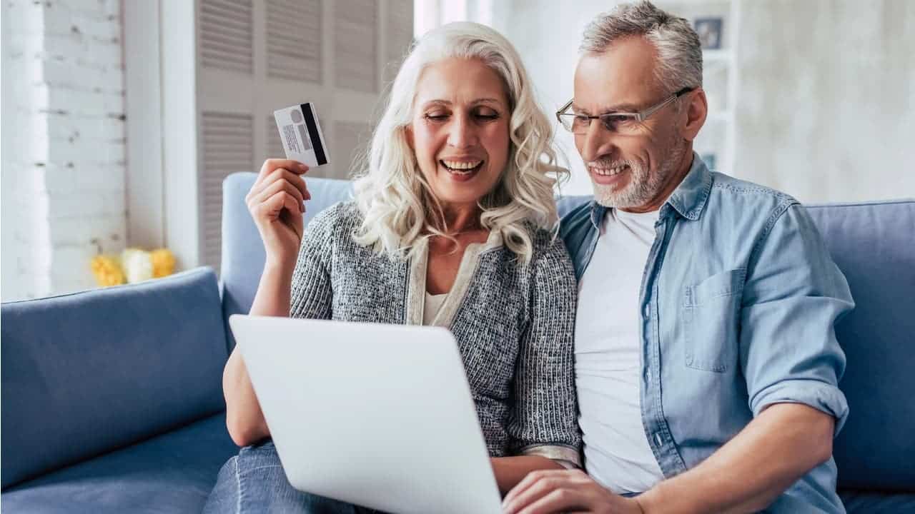Um casal de idosos segurando um cartão em frente a um computador