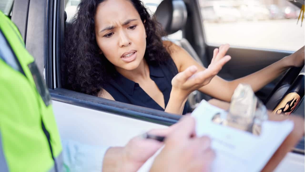 Imagem de uma mulher dentro de carro tomando uma multa de trânsito enquanto dirigia multas