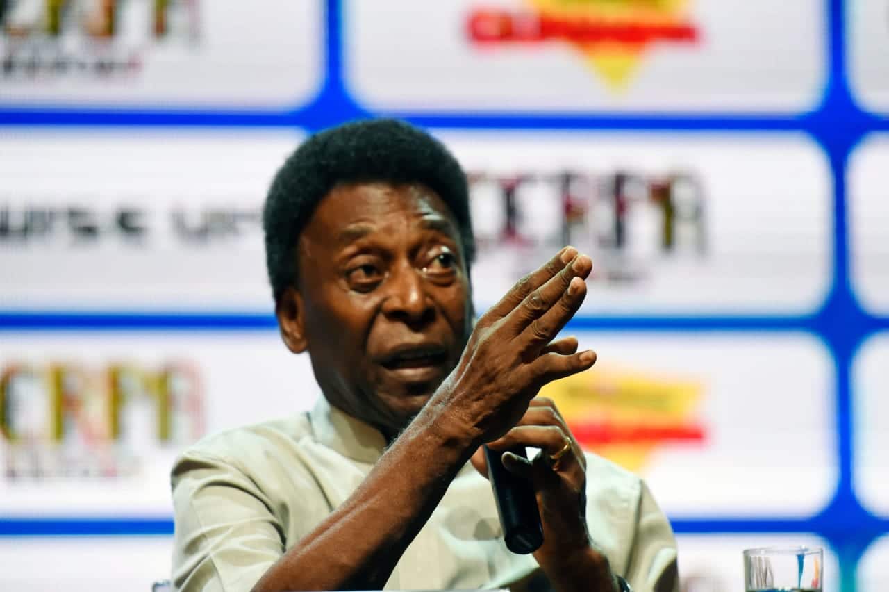 Ex-jogador Pelé fala ao microfone e aponta para frente com sua mão direita