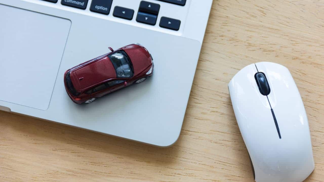 Miniatura de um carro posicionada no canto do teclado de um notebook. Ao lado, um mouse.