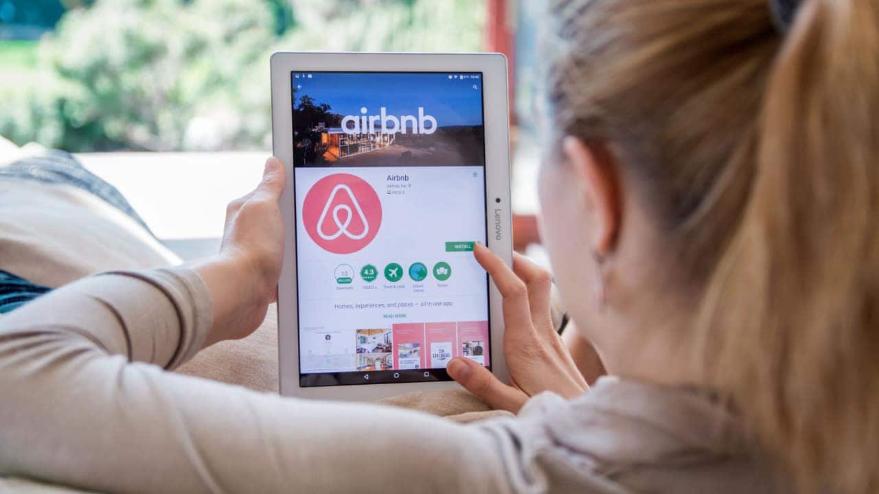imposto de renda Mulher de costas acessando página de download do aplicativo Airbnb por um tablet, e descobrindo como escapar de golpe