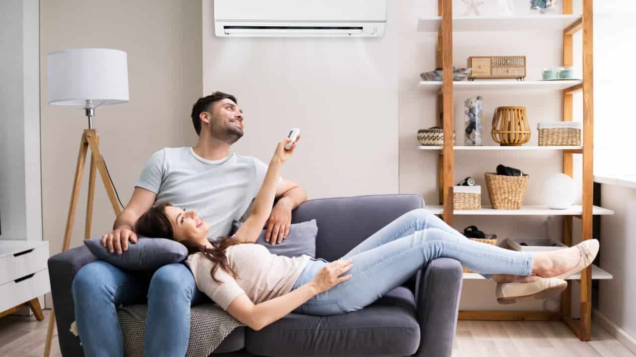 Mulher feliz segurando o controle remoto do condicionador de ar, ao lado do marido no sofá