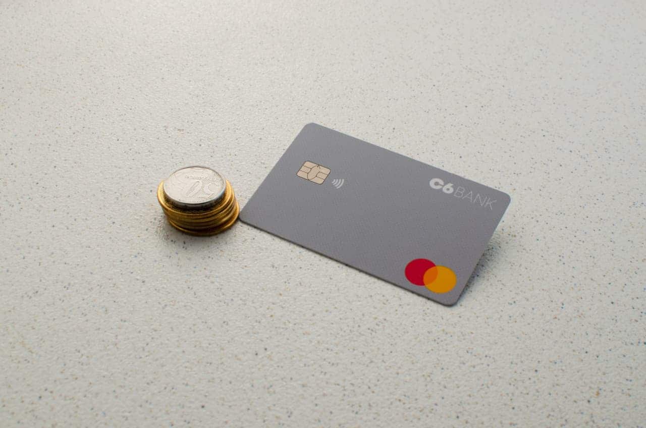 Cartão de crédito do C6 Bank depositado em superfície junto a um montinho de moedas