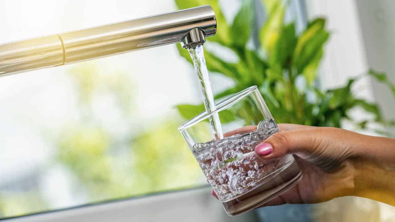 Mão enchendo um copo de água em uma torneira