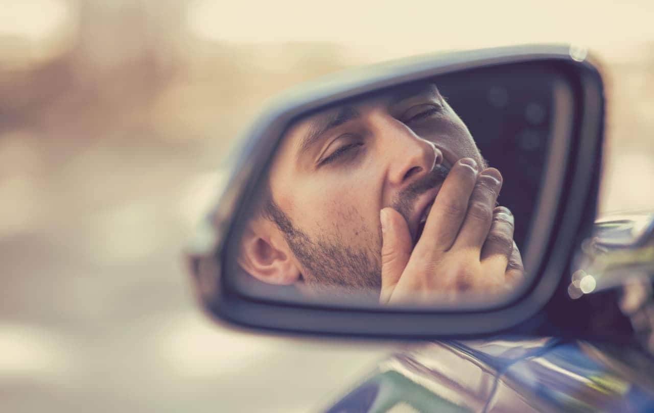 Reflexo de um motorista bocejando no retrovisor de um carro