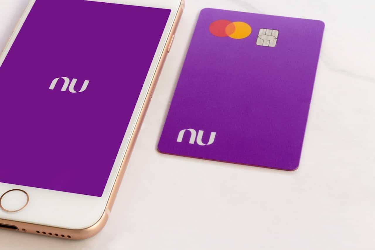 Cartão do Nubank posicionado ao lado de celular que exibe logo da fintech