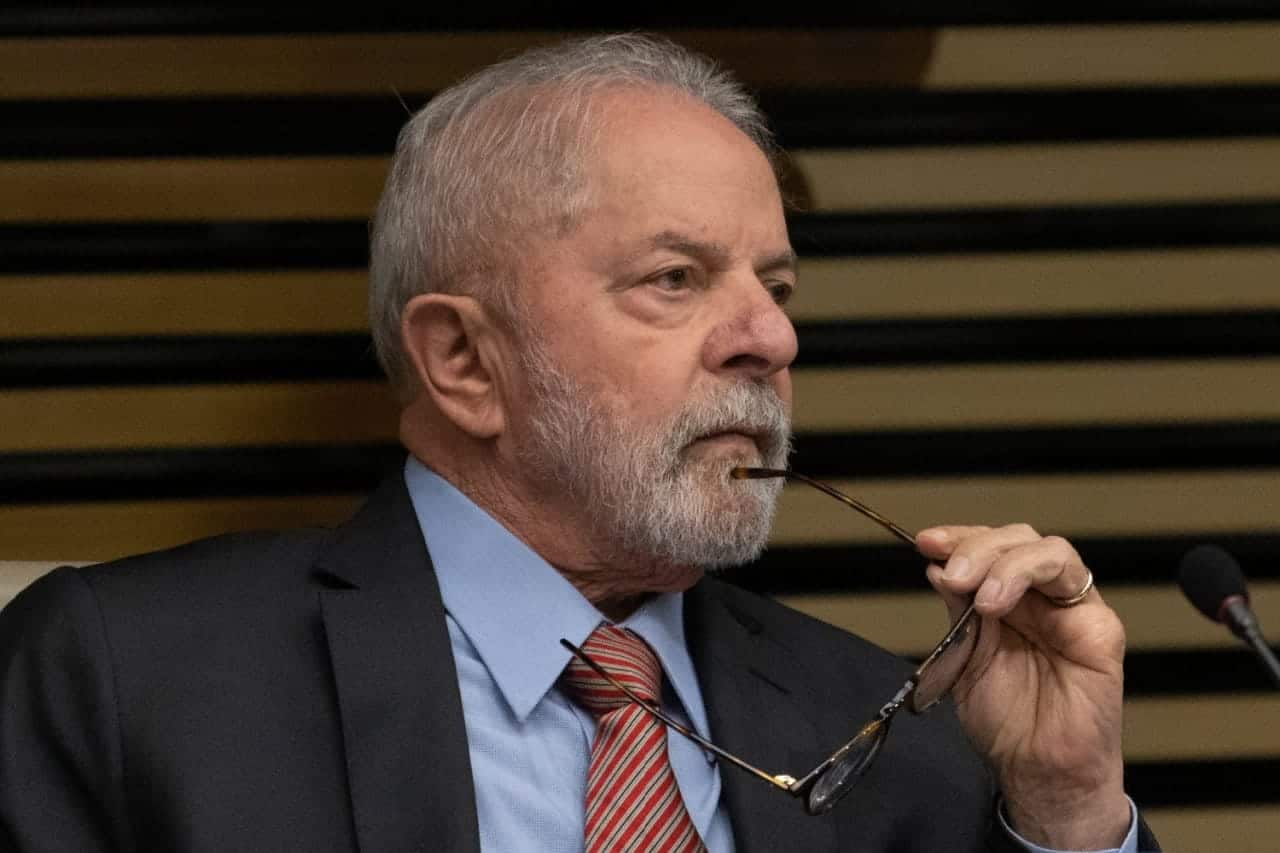 Presidente Lula com expressão séria segurando os óculos na altura do queixo