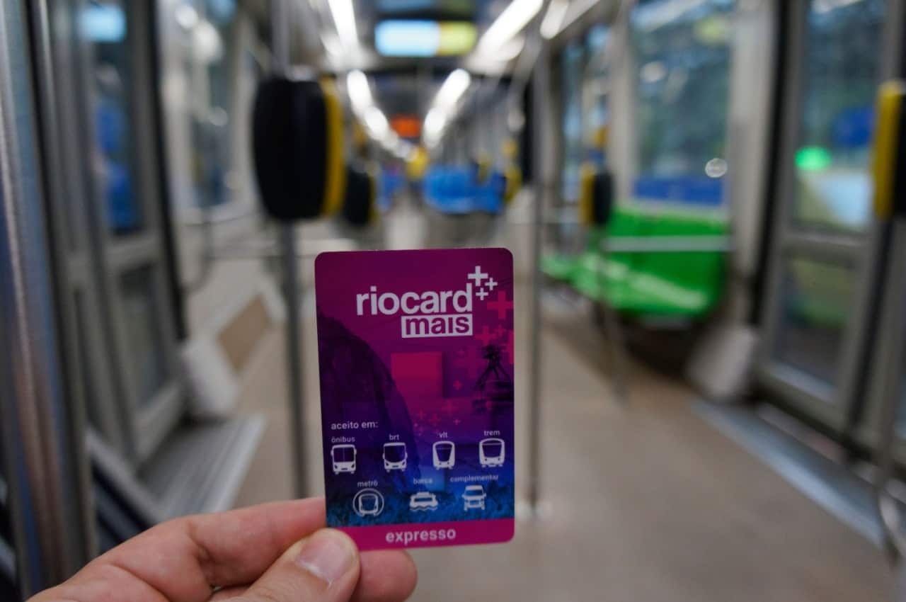 Mão segurando cartão de transporte Riocard Mais.