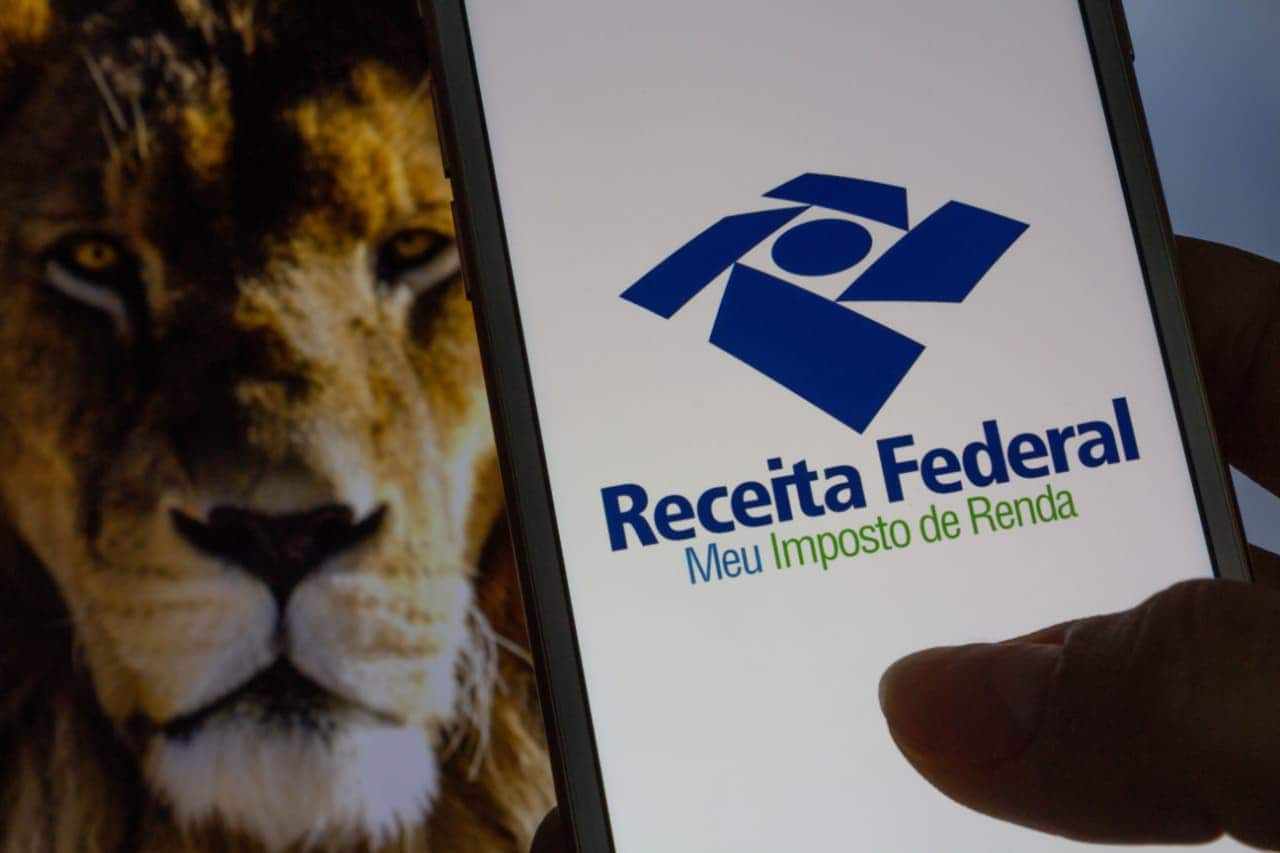 Smartphone aberto no app da Receita Federal e imagem de um leão em segundo plano, ao fundo.
