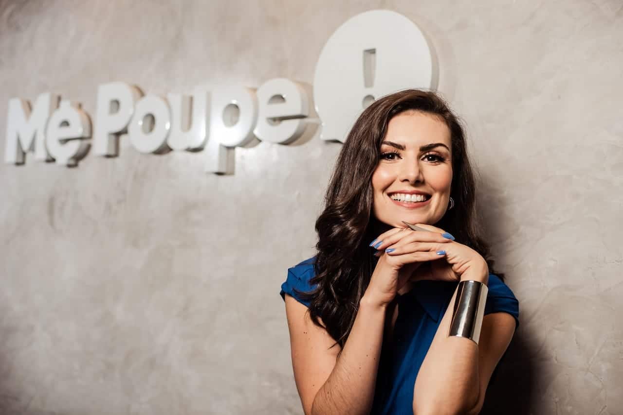 Nathalia Arcuri em frente a uma parede com a escrita "Me Poupe!"