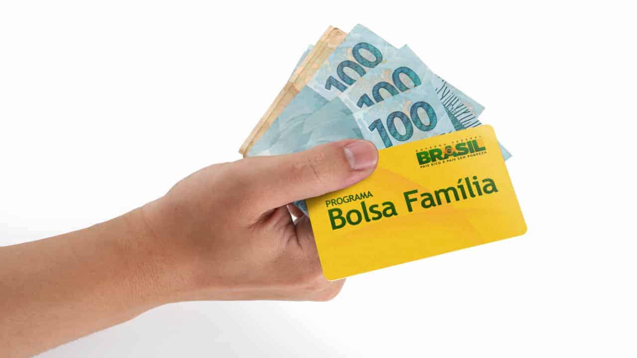Pessoa segurando notas de 100 reais e um cartão do Bolsa Família