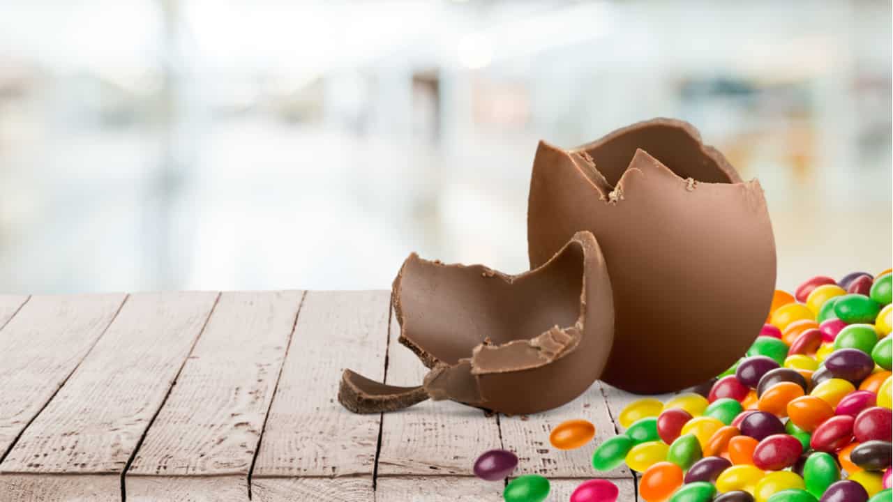 Imagem de um ovo de páscoa partido ao lado de balinhas coloridas