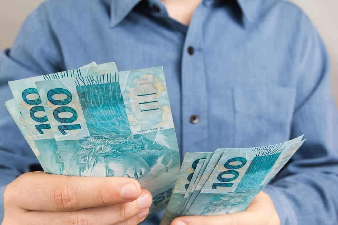 Um homem segurando notas de R$ 100 nas mãos
