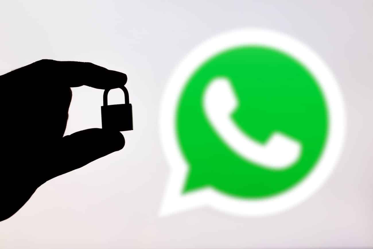Sombra de uma mão segurando um cadeado fechado com símbolo do WhatsApp de fundo