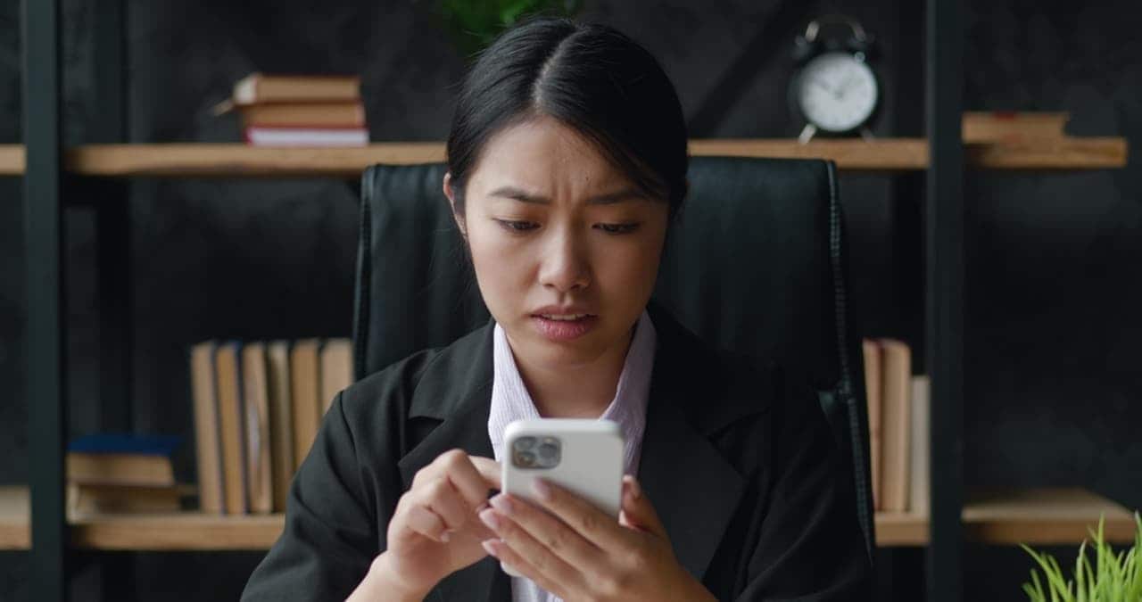 Mulher oriental com expressão preocupada segurando um celular com capinha branca